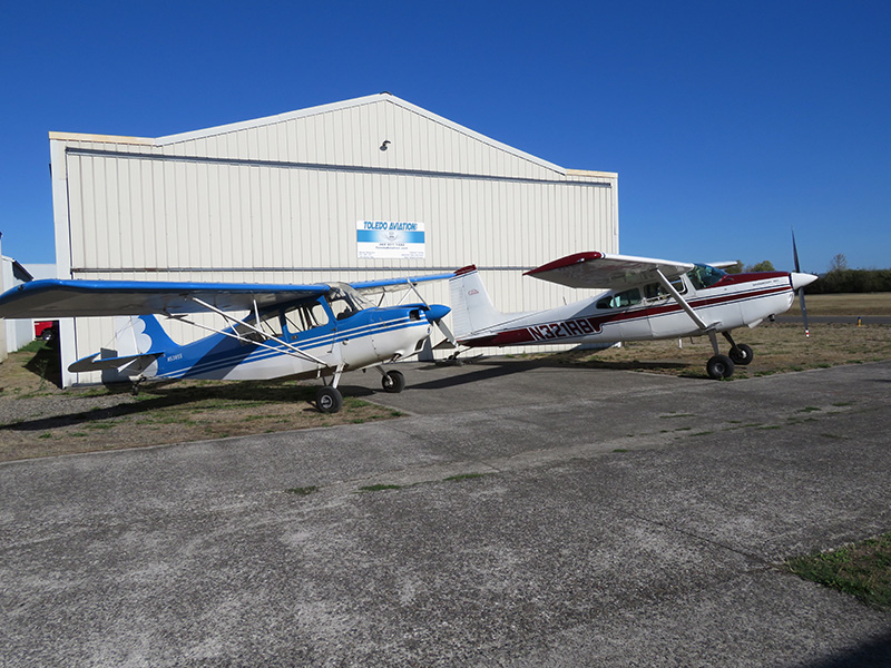 Two small aircraft are parked in front of a hangar at the airport.